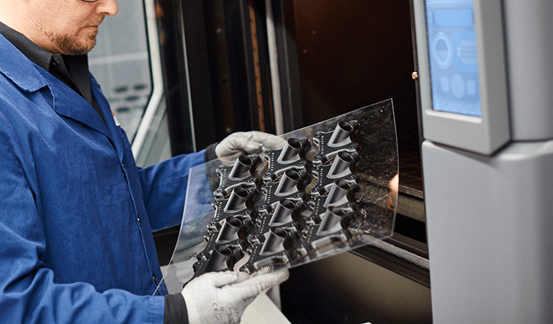 Operatör tar ut färdiga 3D-printade komponenter från Stratasys FDM-skrivare – effektiv produktion av slutprodukter i industriell tillverkning