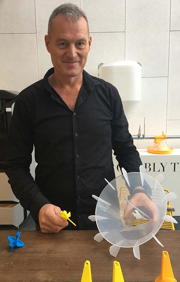 Man i svart skjorta visar upp 3D-printade komponenter utvecklade för användning inom jordbruksindustrin.